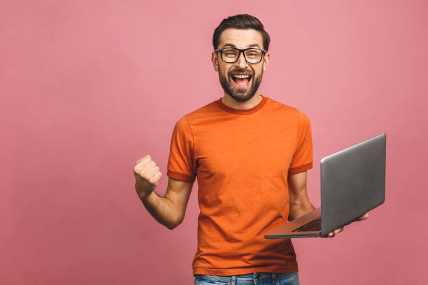 Image of happy excited young man posing isolated over pink background wall using laptop computer make winner gesture.